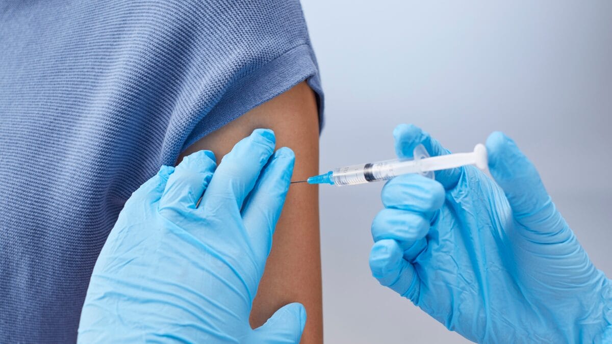 Profissional da saúde usa luvas e aplica vacina em paciente.