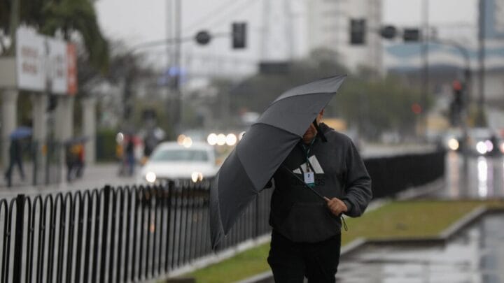Homem caminha na calçada com guarda-chuva.