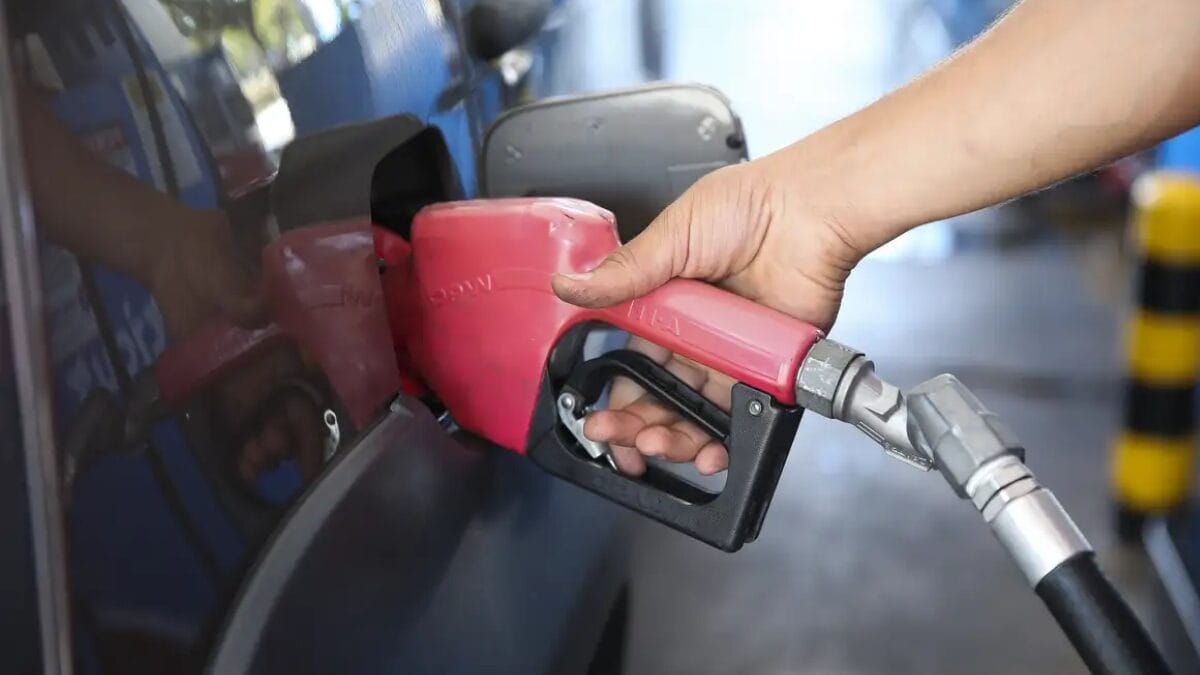 “Mão segurando o bico de uma bomba de combustível enquanto abastece um veículo em um posto de gasolina