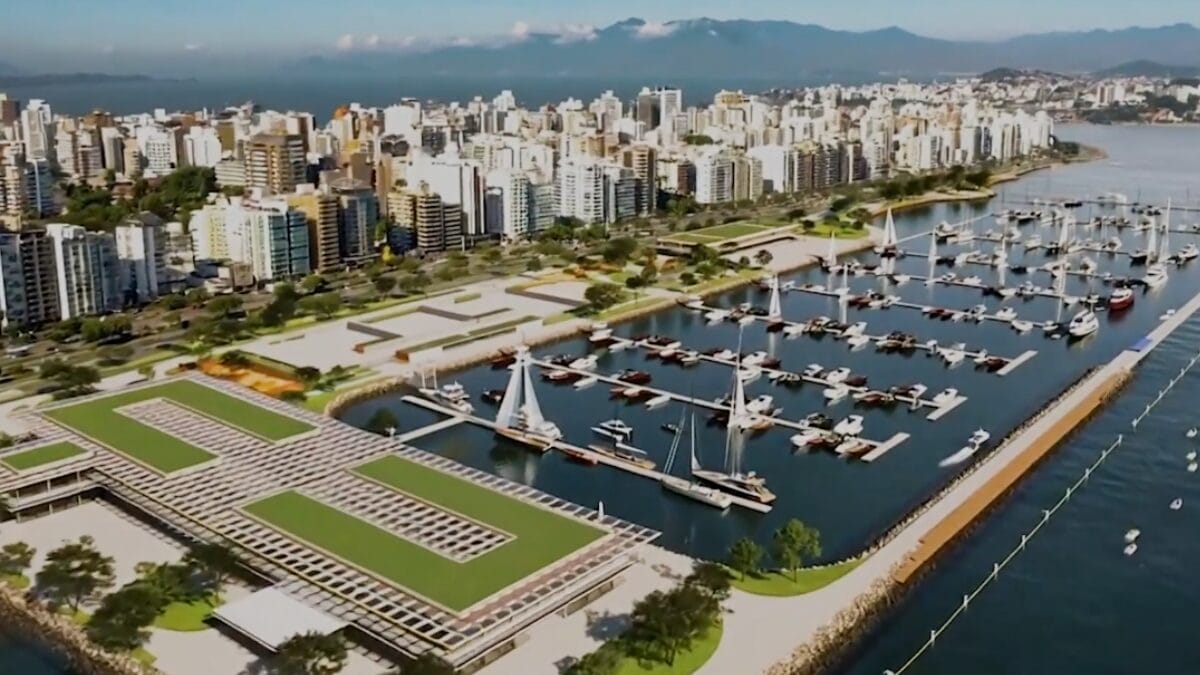 Imagem a&eacute;rea do projeto da Marina e do Parque Urbano da Beira-Mar Norte, com p&iacute;eres, embarca&ccedil;&otilde;es e &aacute;reas verdes integradas &agrave; orla central de Florian&oacute;polis.
