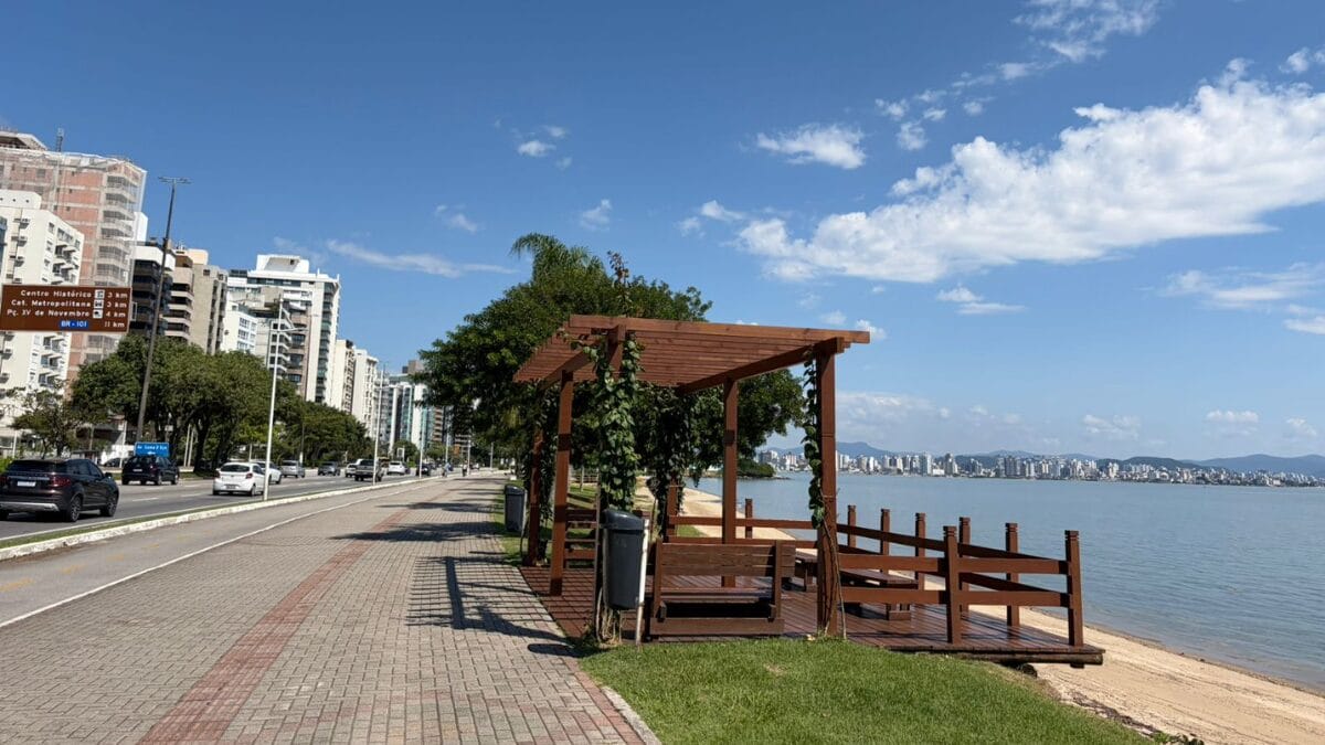 Deck de madeira com pergolado na Beira-Mar Norte, ao lado do cal&ccedil;ad&atilde;o e com vista para o mar e pr&eacute;dios da regi&atilde;o central.