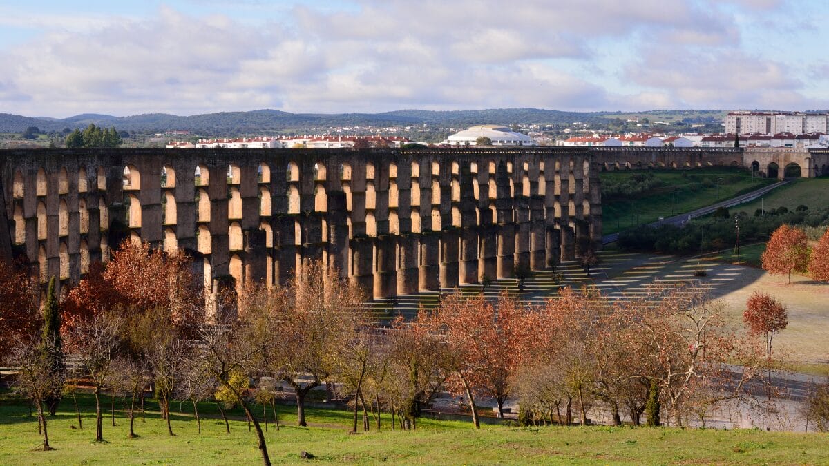 Vista lateral do Aqueduto da Amoreira em Elvas, mostrando suas m&uacute;ltiplas arcadas de pedra sobrepostas que se estendem pela paisagem sob um c&eacute;u nublado.