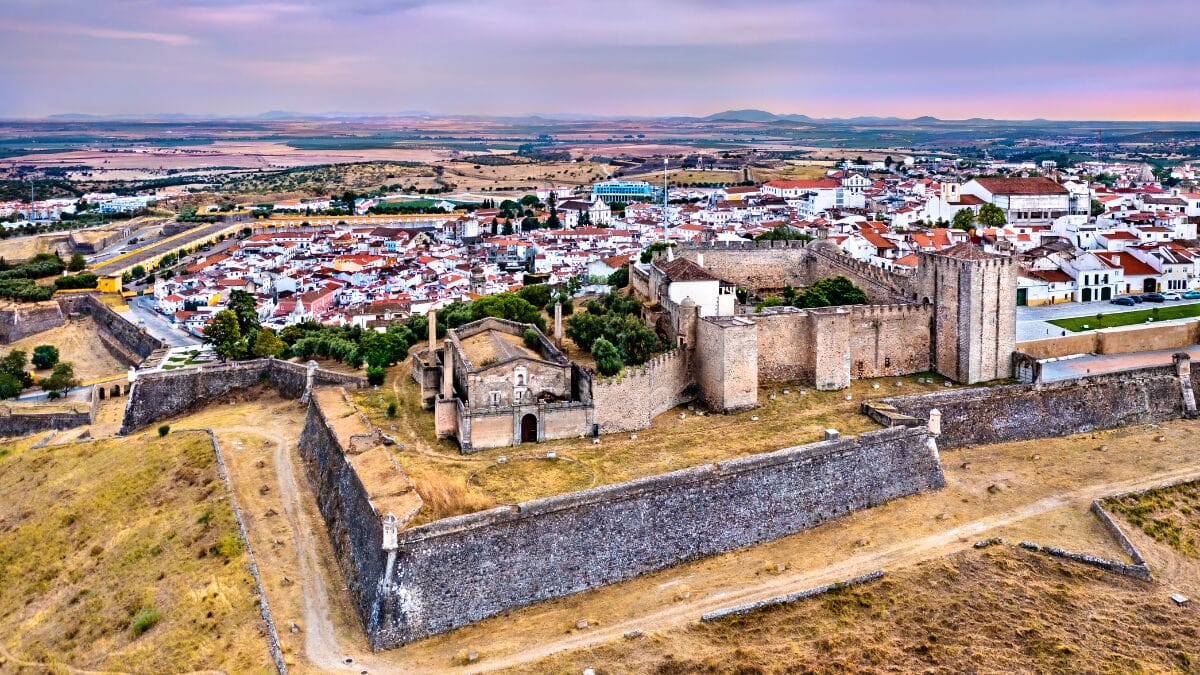 Vista a&eacute;rea aproximada do Castelo de Elvas e suas muralhas de pedra, com a cidade branca ao fundo e oliveiras nos arredores.