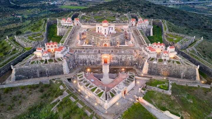 Vista aérea aproximada da parte central do Forte de Nossa Senhora da Graça, iluminado ao entardecer, revelando a casa do governador e os baluartes internos.