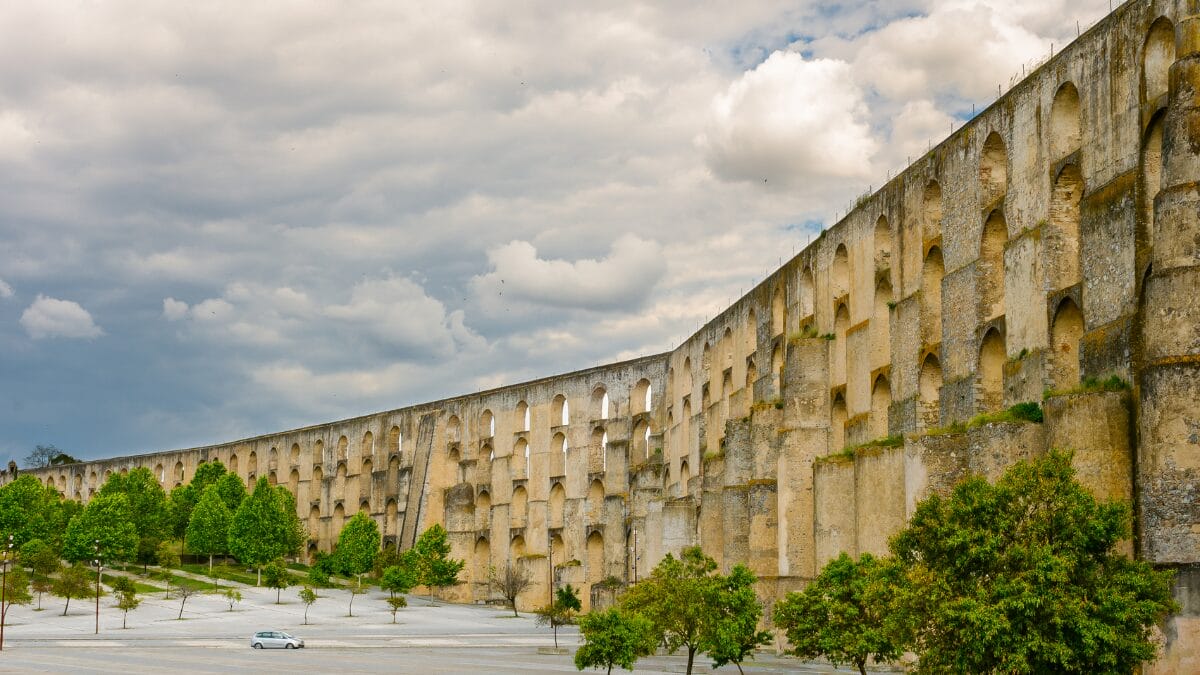 Vista frontal do Aqueduto da Amoreira atravessando um vale verde com &aacute;rvores de folhas alaranjadas no outono.