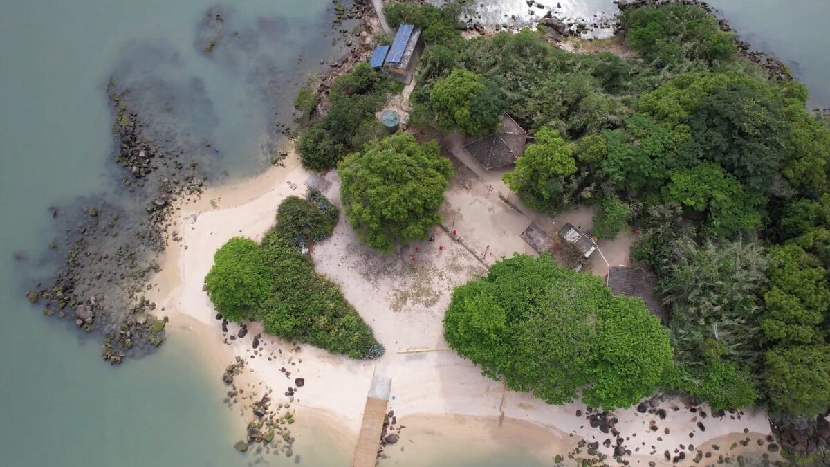 Vista a&eacute;rea da Ilha dos Guar&aacute;s Grande, com faixas de areia claras, vegeta&ccedil;&atilde;o densa e pequenas constru&ccedil;&otilde;es pr&oacute;ximas &agrave; praia.
