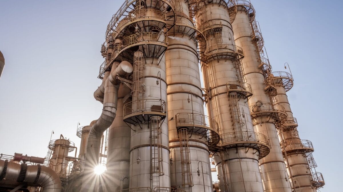 Torres e tubula&ccedil;&otilde;es met&aacute;licas de uma instala&ccedil;&atilde;o industrial, com estrutura elevada e ilumina&ccedil;&atilde;o natural.