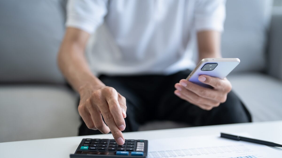 pessoa segurando celular e fazendo contas na calculadora
