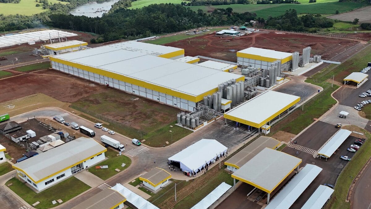 Vista externa da f&aacute;brica com galp&otilde;es industriais e estrutura de apoio.