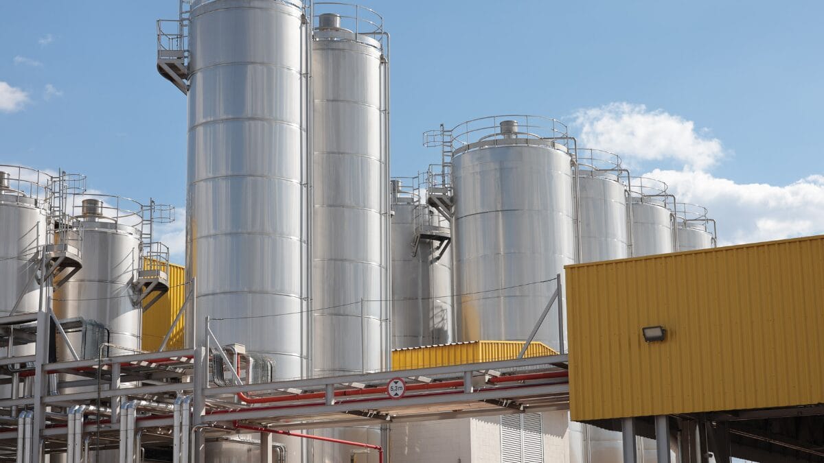 Grandes tanques cil&iacute;ndricos de a&ccedil;o inox instalados na &aacute;rea externa da ind&uacute;stria.