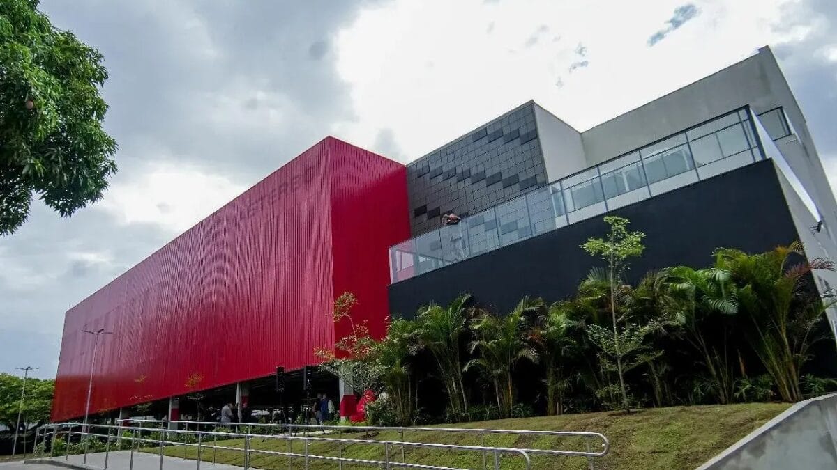 Vista externa de um pr&eacute;dio industrial moderno da Masterboi, com fachada vermelha e preta, cercado por &aacute;rea verde e acesso pavimentado.
