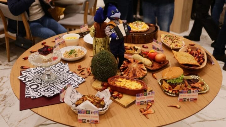 Pratos apresentados no Festival Sabores da Serra, dispostos em uma mesa redonda com um enfeite de gralhas no centro
