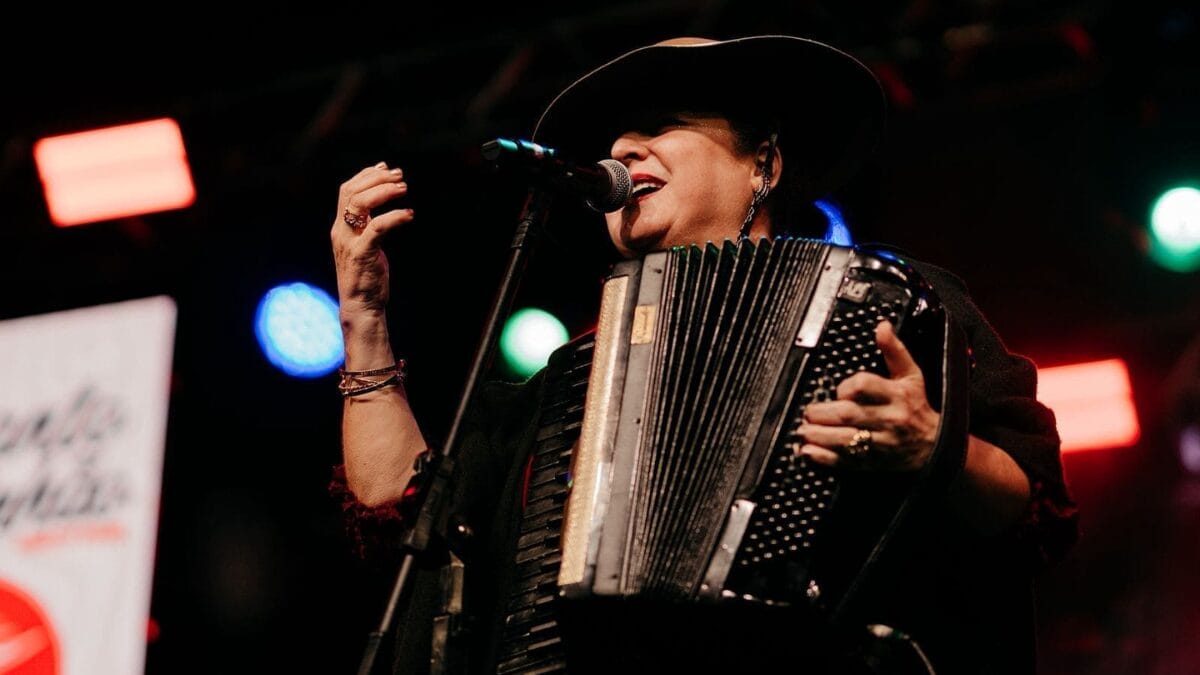 Cantora Cássia Abreu com chapéu, cantando e tocando gaita