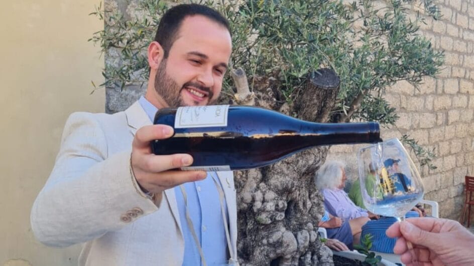 Homem branco de terno claro servindo um vinho