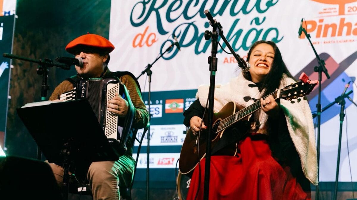 Os artistas Paulinho Guazzelli e Ana Leart, respectivamente, sentados e vestidos com trajes tradicionais do sul do Brasil