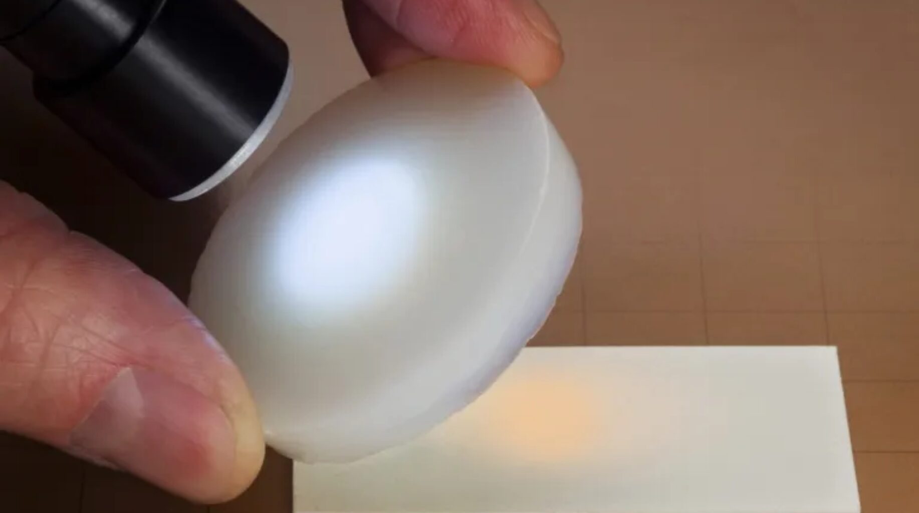 Pedra de aerogel branco iluminada por lanterna, mostrando aspecto translúcido e leve do material