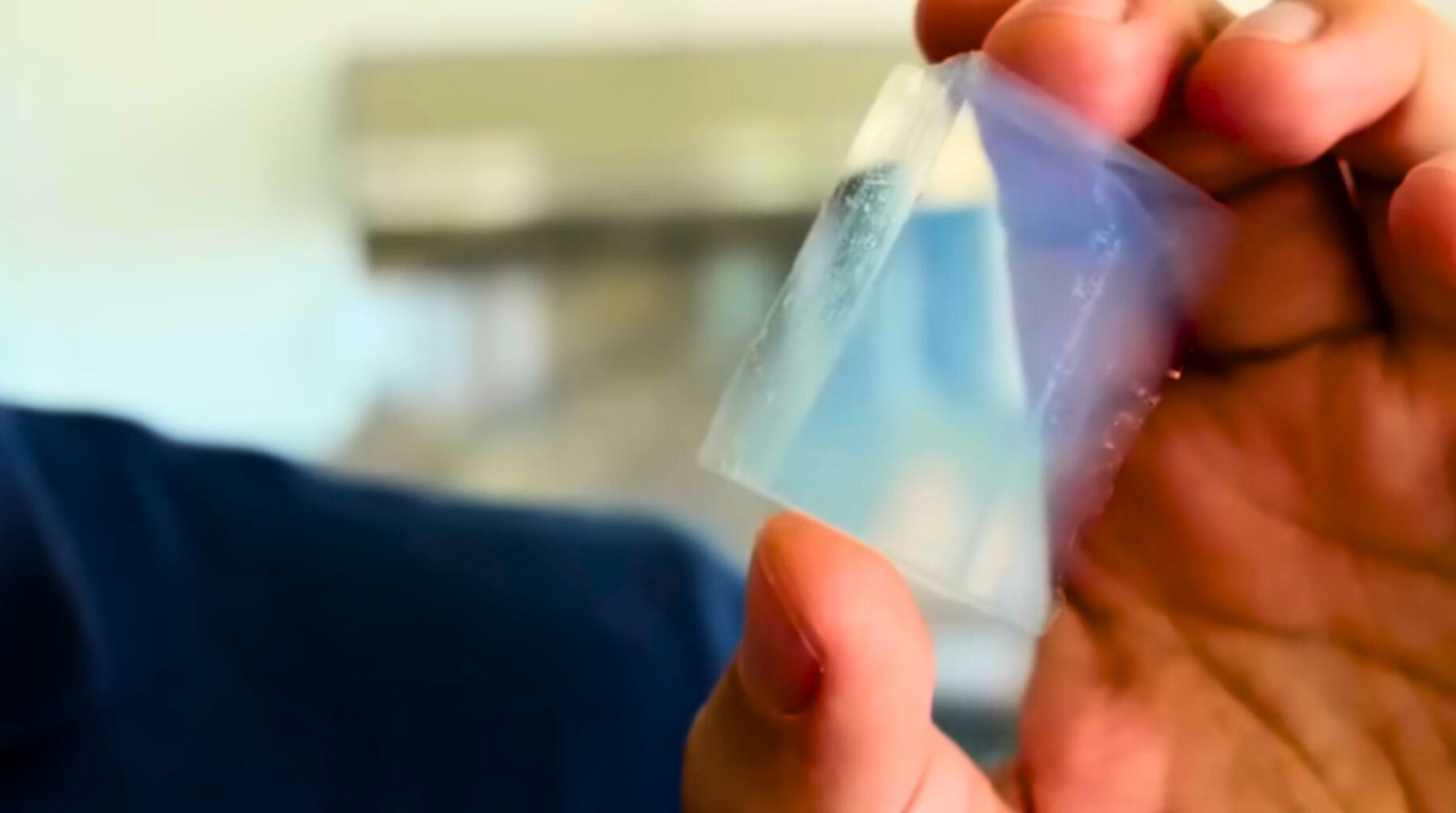 Close-up de pedaço de aerogel azul translúcido entre os dedos, evidenciando o Efeito Rayleigh