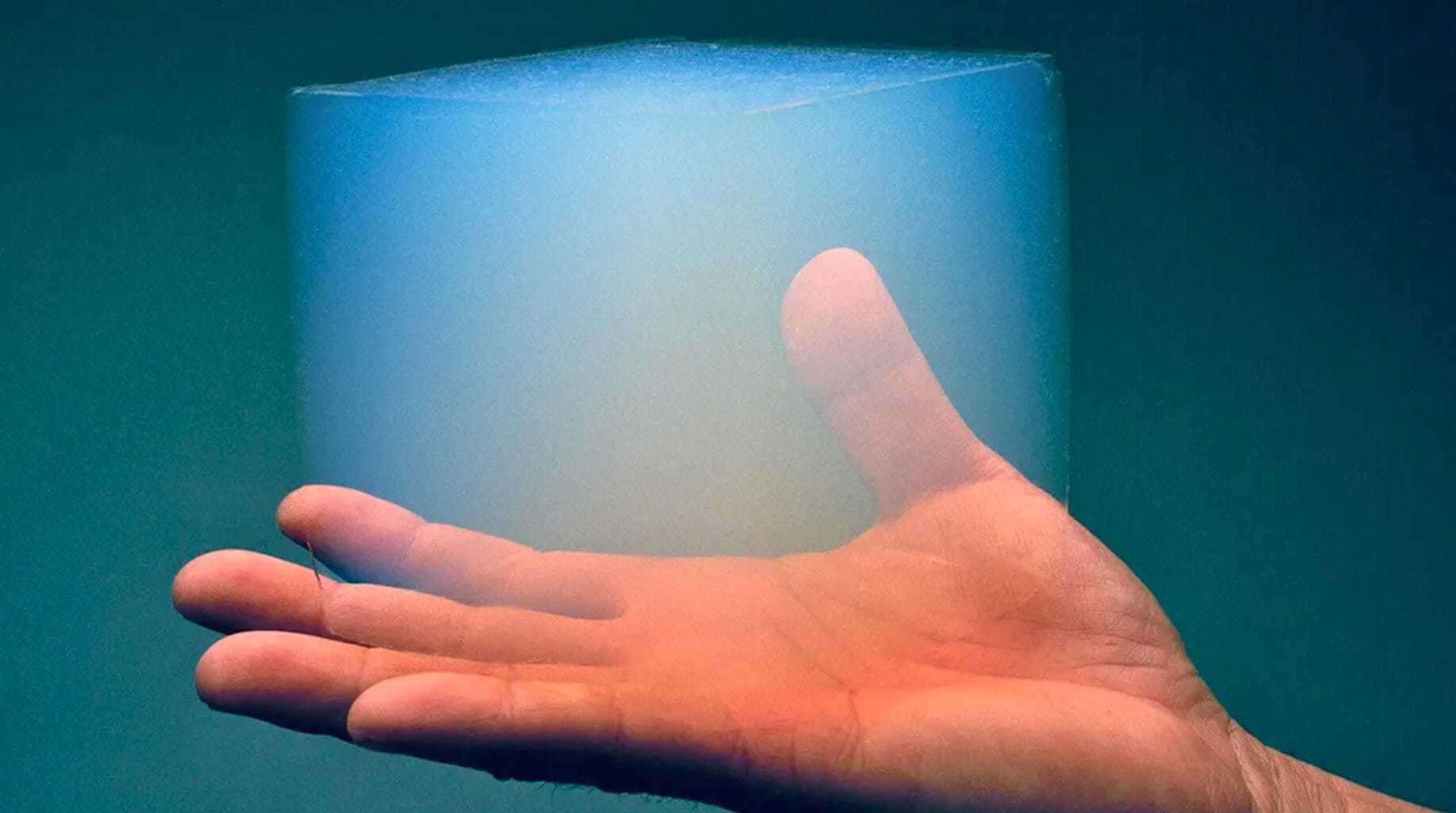 Mão segurando um cubo de aerogel azul translúcido, material 99% ar usado pela NASA