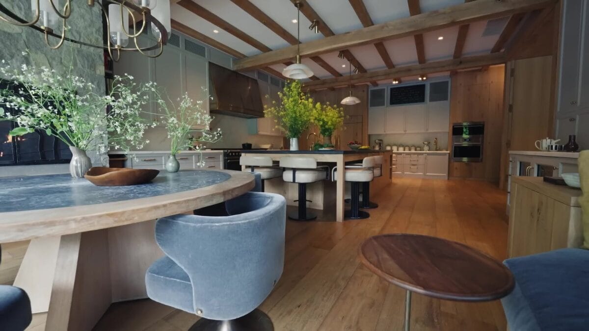 &Aacute;rea de jantar integrada &agrave; cozinha, com mesa branca, cadeiras curvas azul-claras, teto inclinado em madeira e janelas amplas voltadas para o jardim.