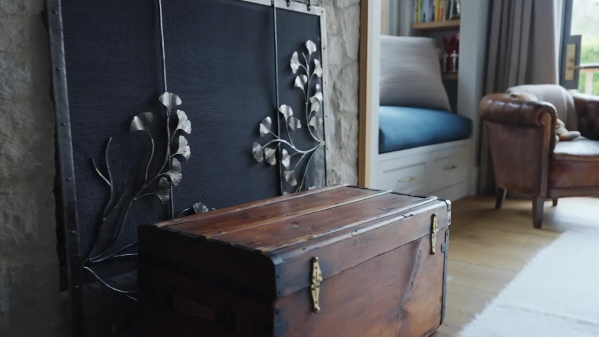 Quarto principal com cama king de cabeceira estofada azul-petr&oacute;leo e colcha do mesmo tom, ba&uacute; antigo de madeira aos p&eacute;s da cama e cortinas claras nas janelas amplas.