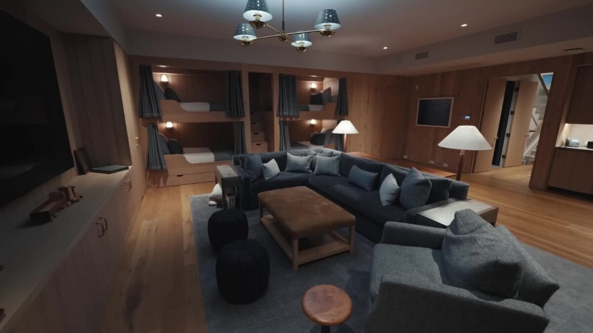Sala de cinema em casa com sof&aacute; seccional cinza em U, alcovas com cortinas e abajures em cada nicho, paredes e teto revestidos em madeira clara.