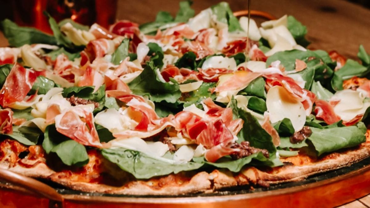 Pizza com cobertura farta de folhas de rúula, nozes, presunto parma e queijo, da Di Pietre.