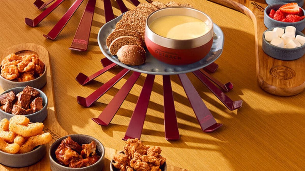 Fondue do Outback com recipientes de queijo derretido, porções de carnes, frutas e fritas.