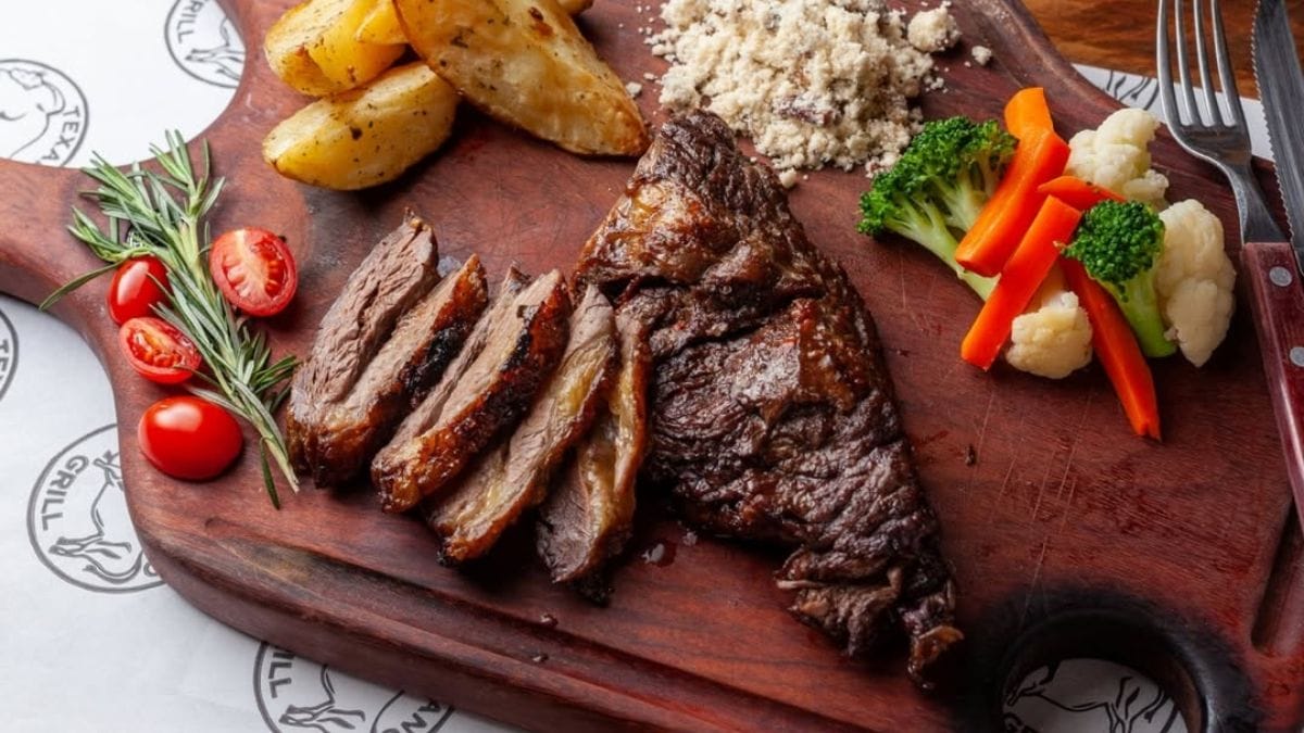 Tábua com porção de carne bovina assada e cortada acompanhada de batas e legumes, do Texano Grill.
