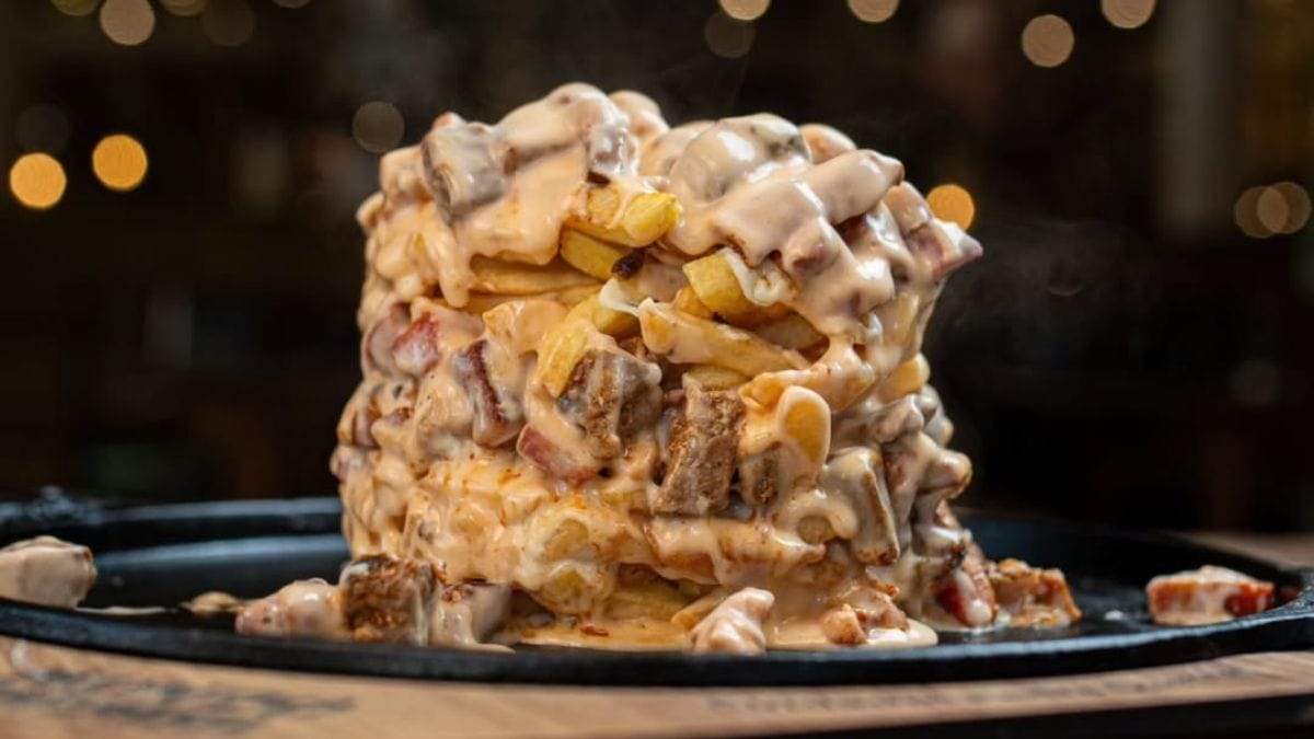 Torre de batatas fritas coberta com queijo derretido e pedaços de carne.