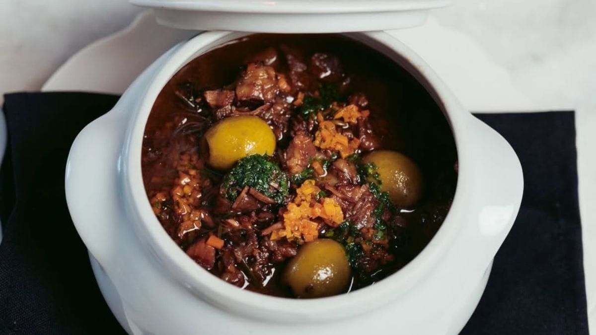 Carne de panela com molho, especiarias e azeitonas verdes, servidas em panela de ceramica branca, do Beau Social Club.