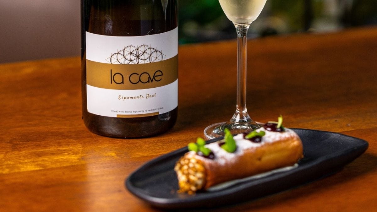 Doce em formato de rolinho disposto em uma mesa de madeira, servido junto com espumante La Cave.