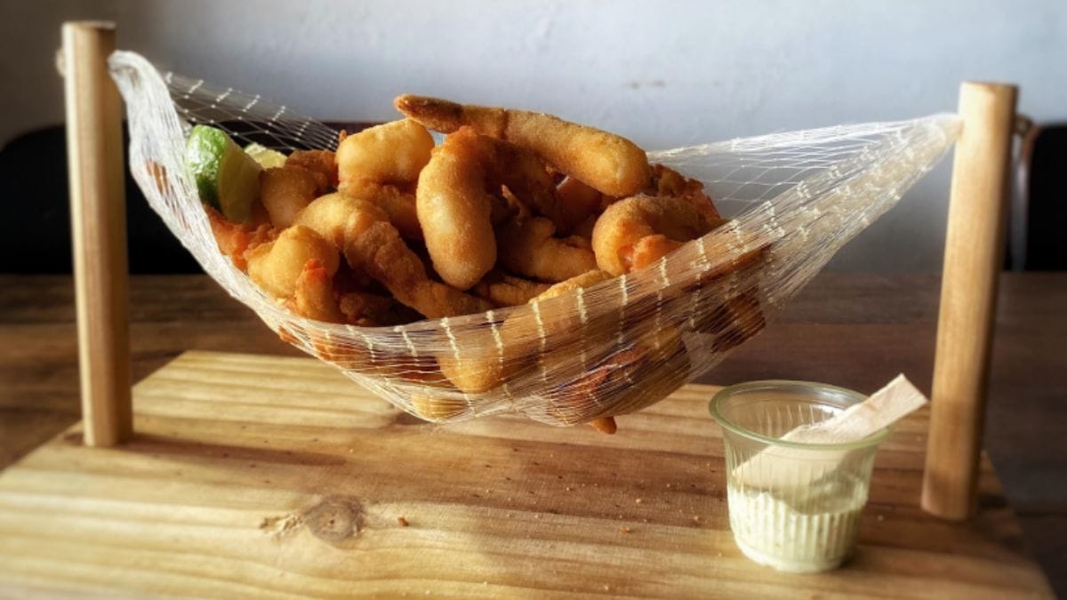 Porção de camarões empanados e fritos disposta uma rede em miniatura decorativa, do Boteco Zé Mané.