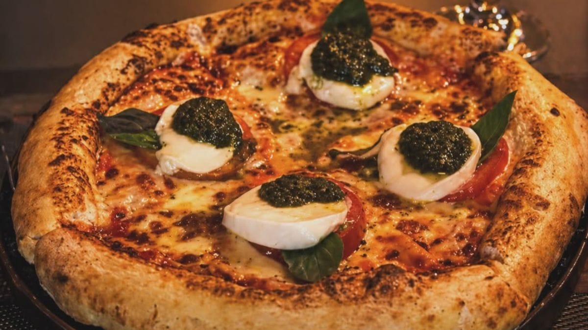 Pizza inteira coberta com queijo, manjericão, molho pesto e tomate, da El Padre.