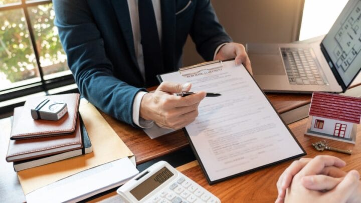 pessoa de terno mostra contrato para assinatura em uma mesa com calculadora e notebook