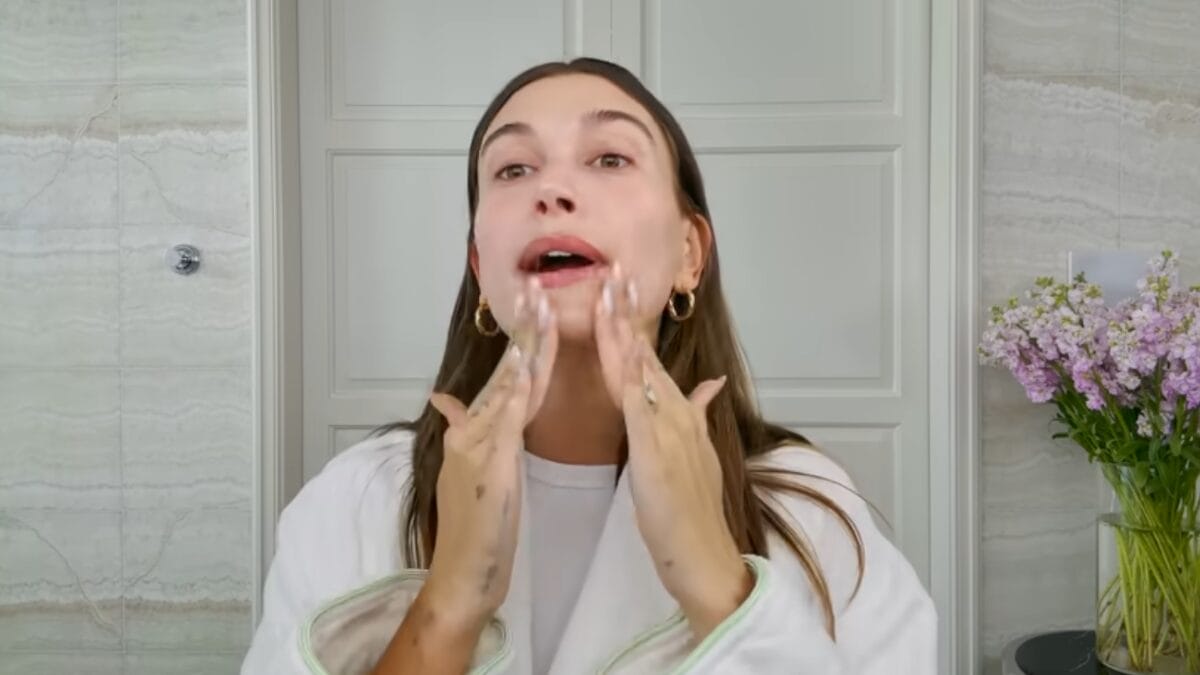 Hailey Bieber aplica produto hidratante no rosto durante rotina matinal de skincare.