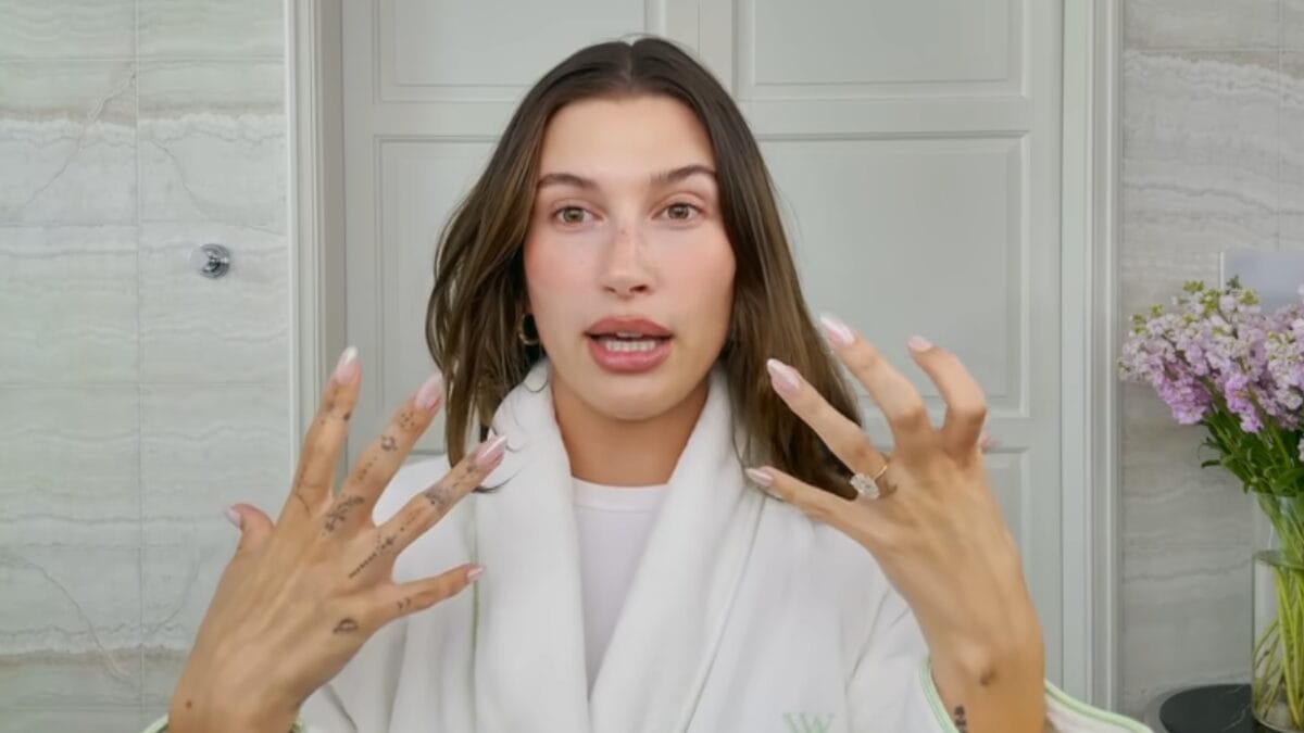 Hailey Bieber mostra as m&atilde;os enquanto explica detalhes da rotina de maquiagem leve.