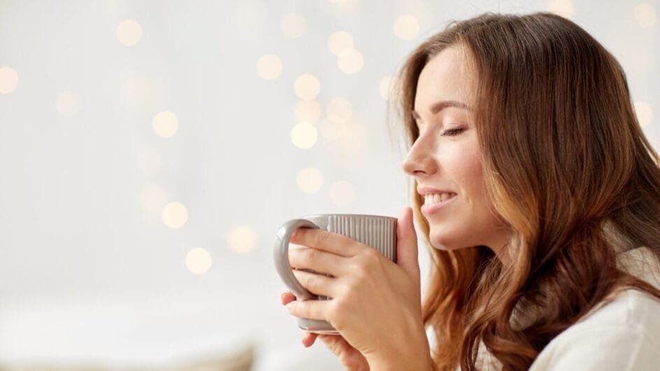 Mulher segurando uma caneca quente e sorrindo em ambiente aconchegante.