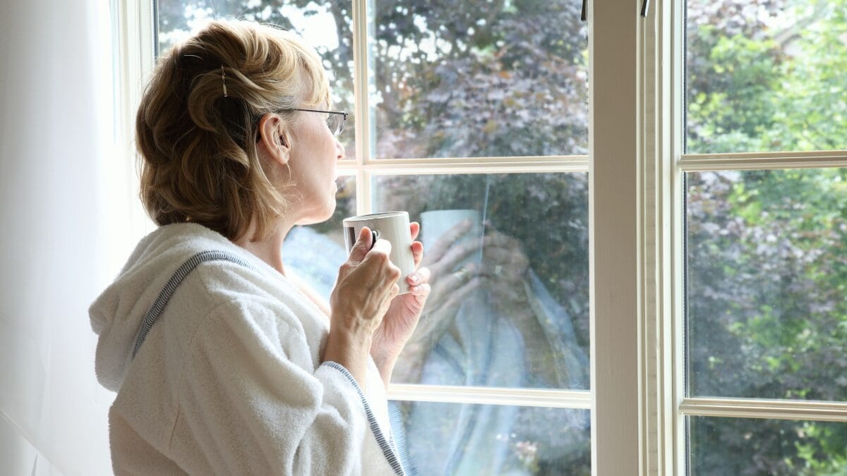 Mulher observando a paisagem pela janela enquanto segura uma xícara de café.