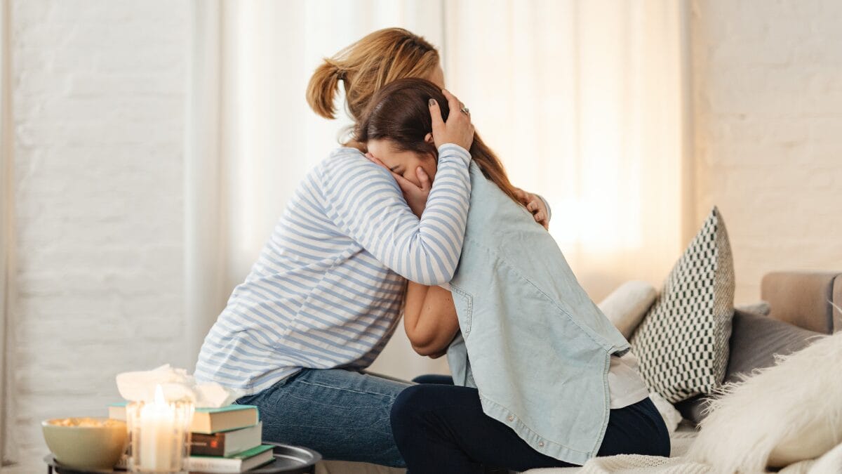 Mulher abraçando outra pessoa em gesto de apoio emocional dentro de casa.