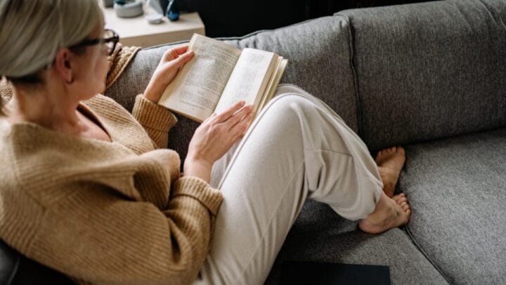 Mulher sentada no sofá lendo um livro em momento de descanso e conforto dentro de casa.