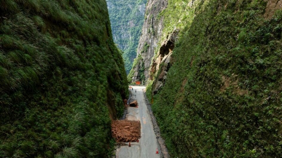 estrada em obras cercada por paredões de rocha e vegetação