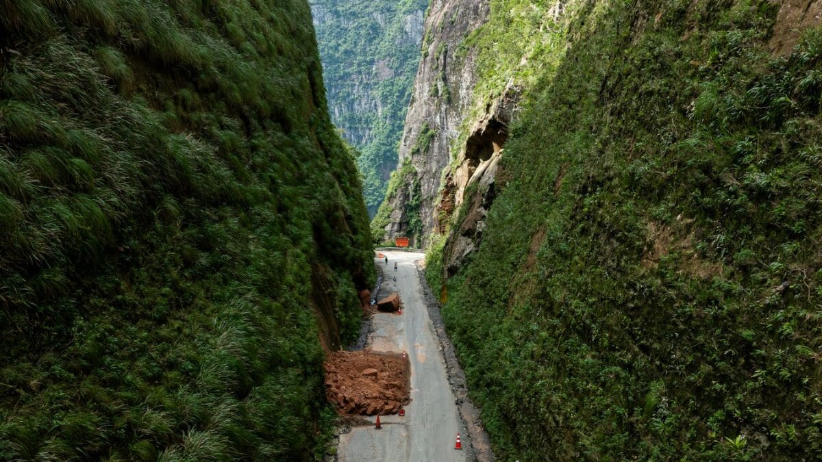 estrada em obras cercada por paredões de rocha e vegetação