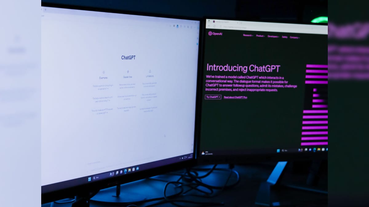 Duas telas de monitores exibindo linhas de diálogo de inteligência artificial em uma sala escura de escritório