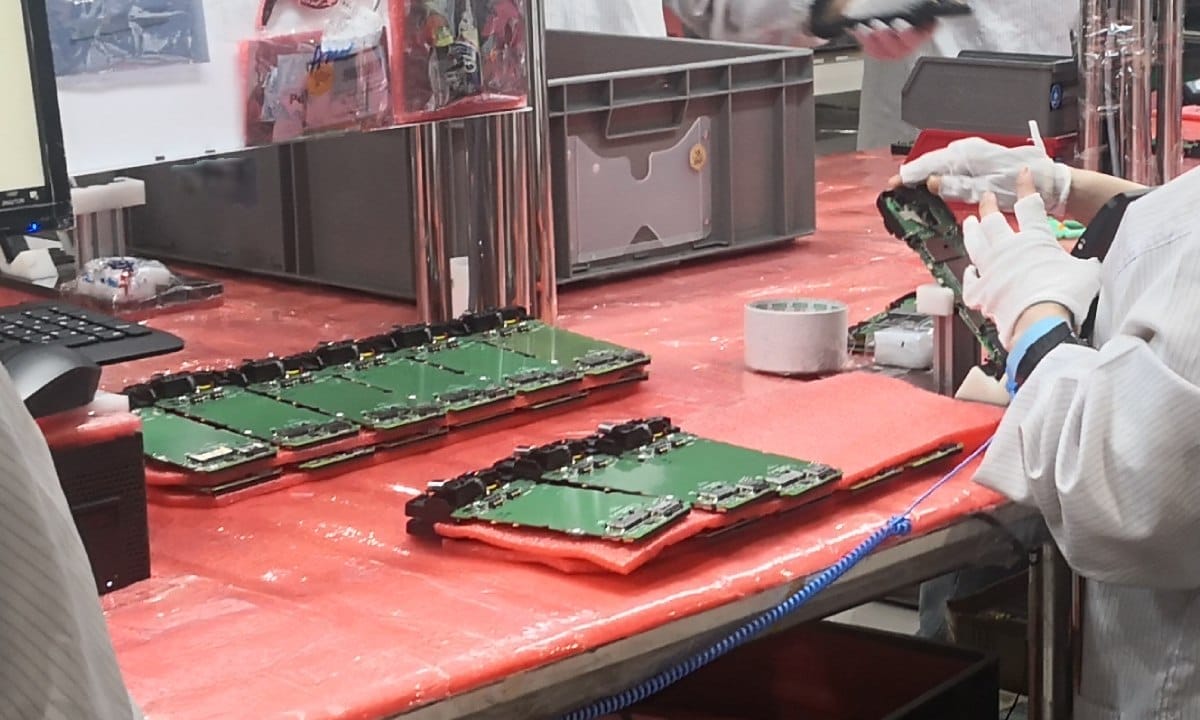 Trabalhadores ajustam componentes de smartphone manualmente em f&aacute;brica