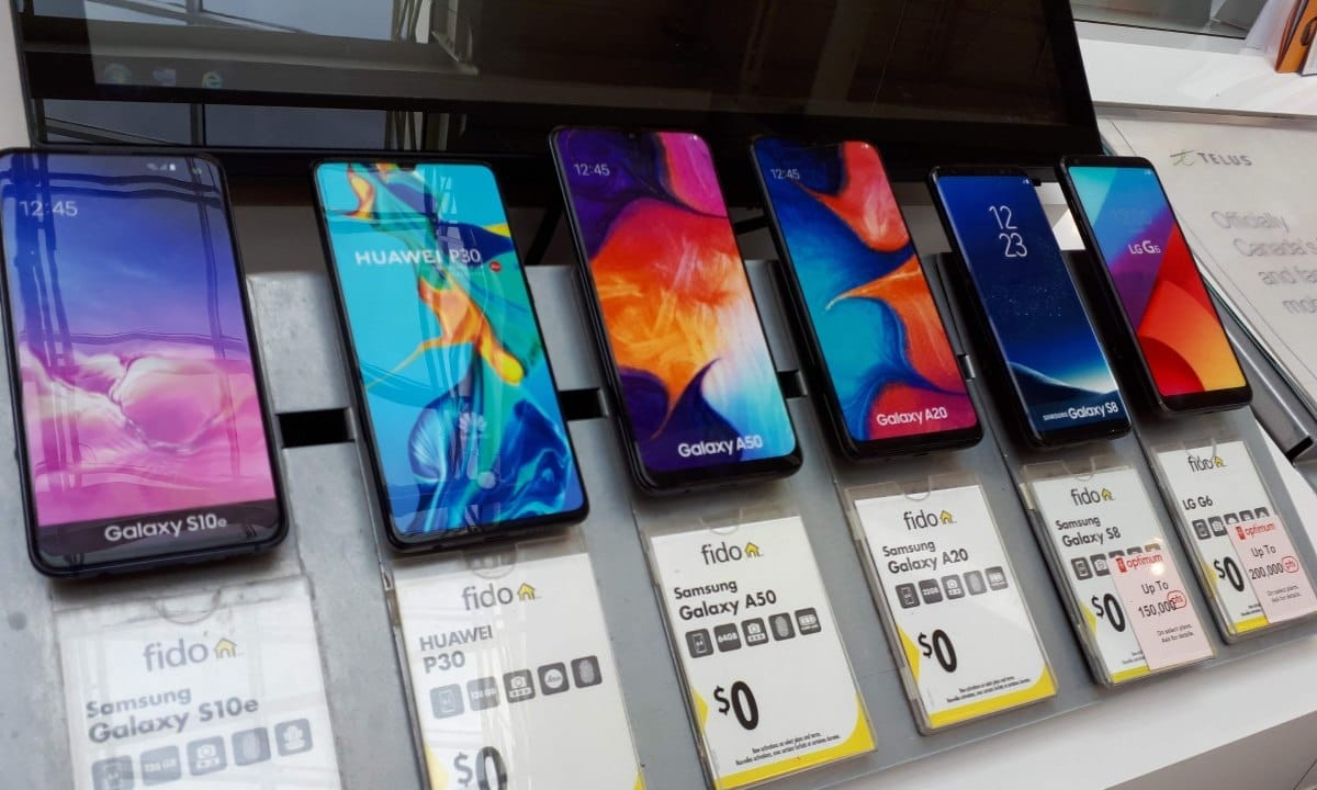 Fileira de smartphones modernos de diversas marcas expostos em uma mesa de madeira em uma loja de tecnologia