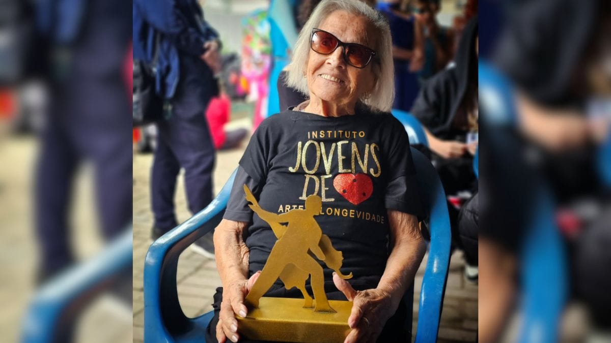 Festival de Dança de Joinville: foto da Dona Maura sentada, segurando o troféu