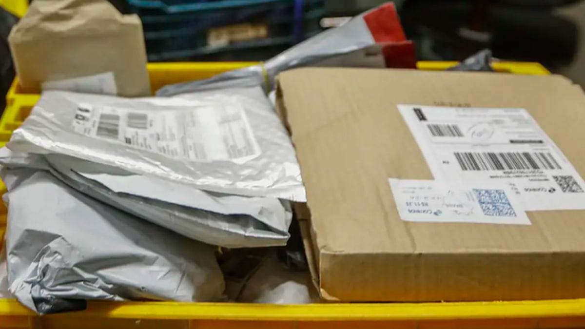 Pacotes de compras internacionais e caixas de papelão empilhados em um cesto amarelo dos Correios, representando o fluxo de mercadorias afetadas pela taxa das blusinhas.