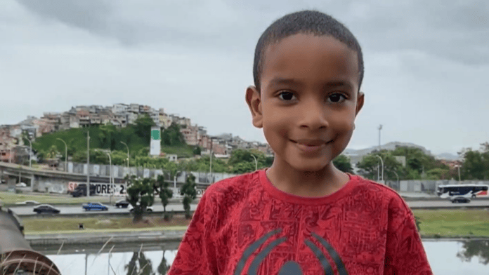 Alvinho é fotografado em uma área da Maré, com a comunidade ao fundo. (Foto: Reprodução)