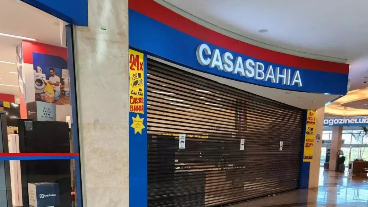 Fachada de uma loja da Casas Bahia dentro de um shopping center com as portas de enrolar metálicas completamente fechadas, ilustrando o fechamento de unidades em meio à crise financeira da rede varejista.
