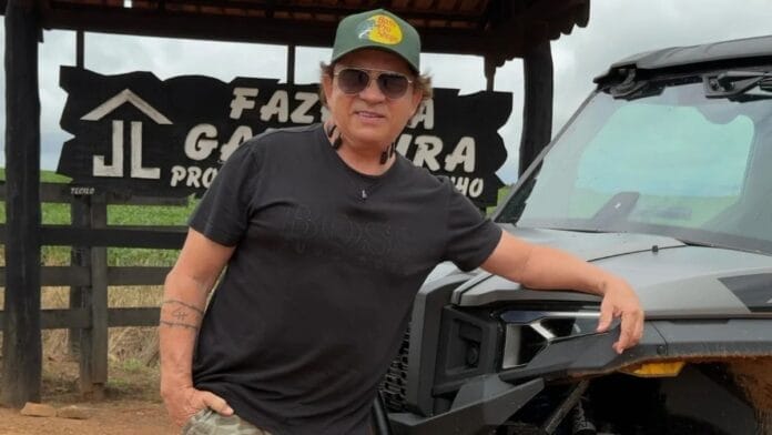 Chitãozinho apoiado em um veículo utilitário na entrada da fazenda, sob a placa de identificação